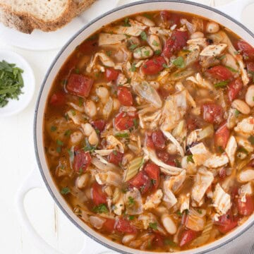 Cabbage and chicken soup with vegetables, cannellini beans, and chicken in a white pot.