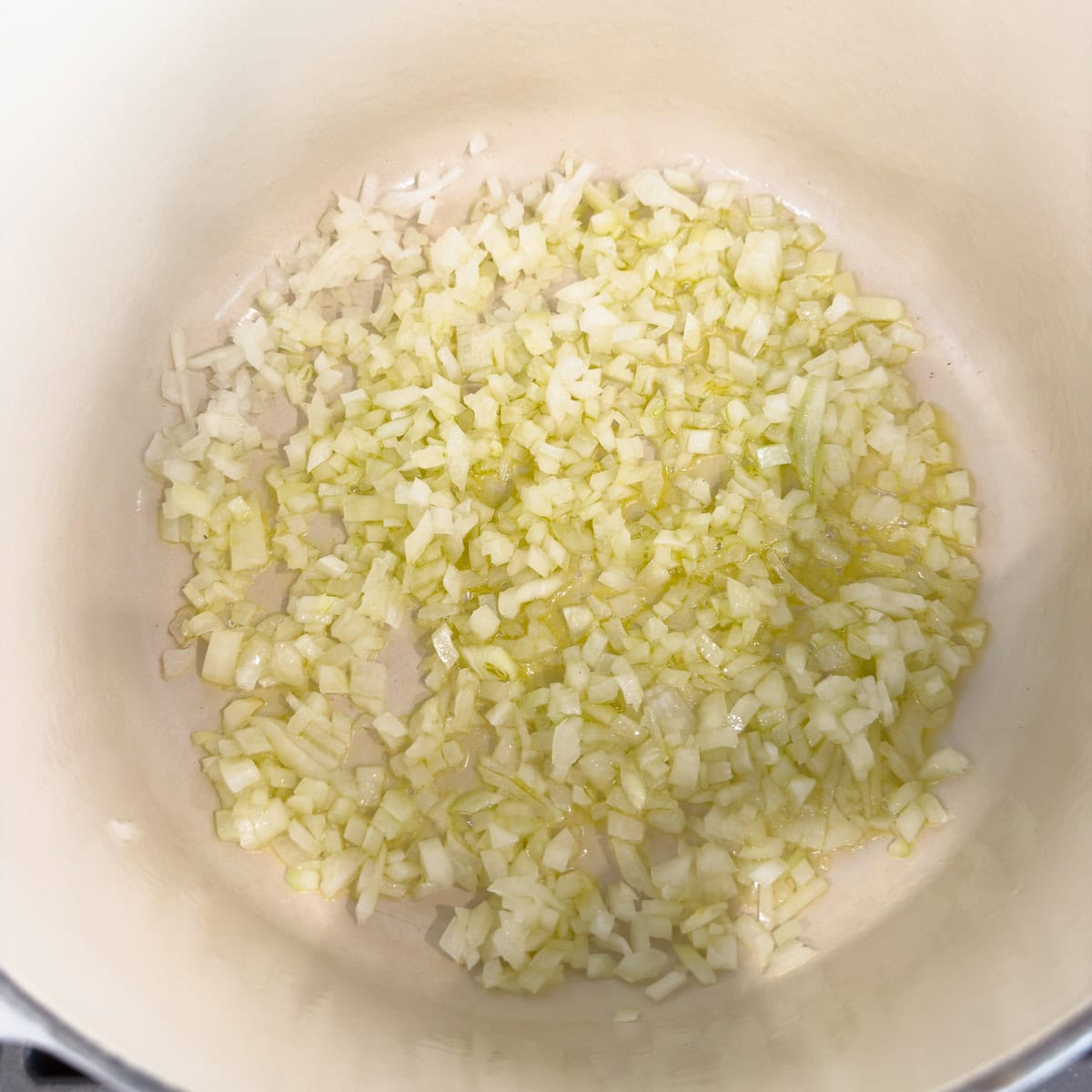 Chopped onion sautéing with oil in a white pot stovetop.