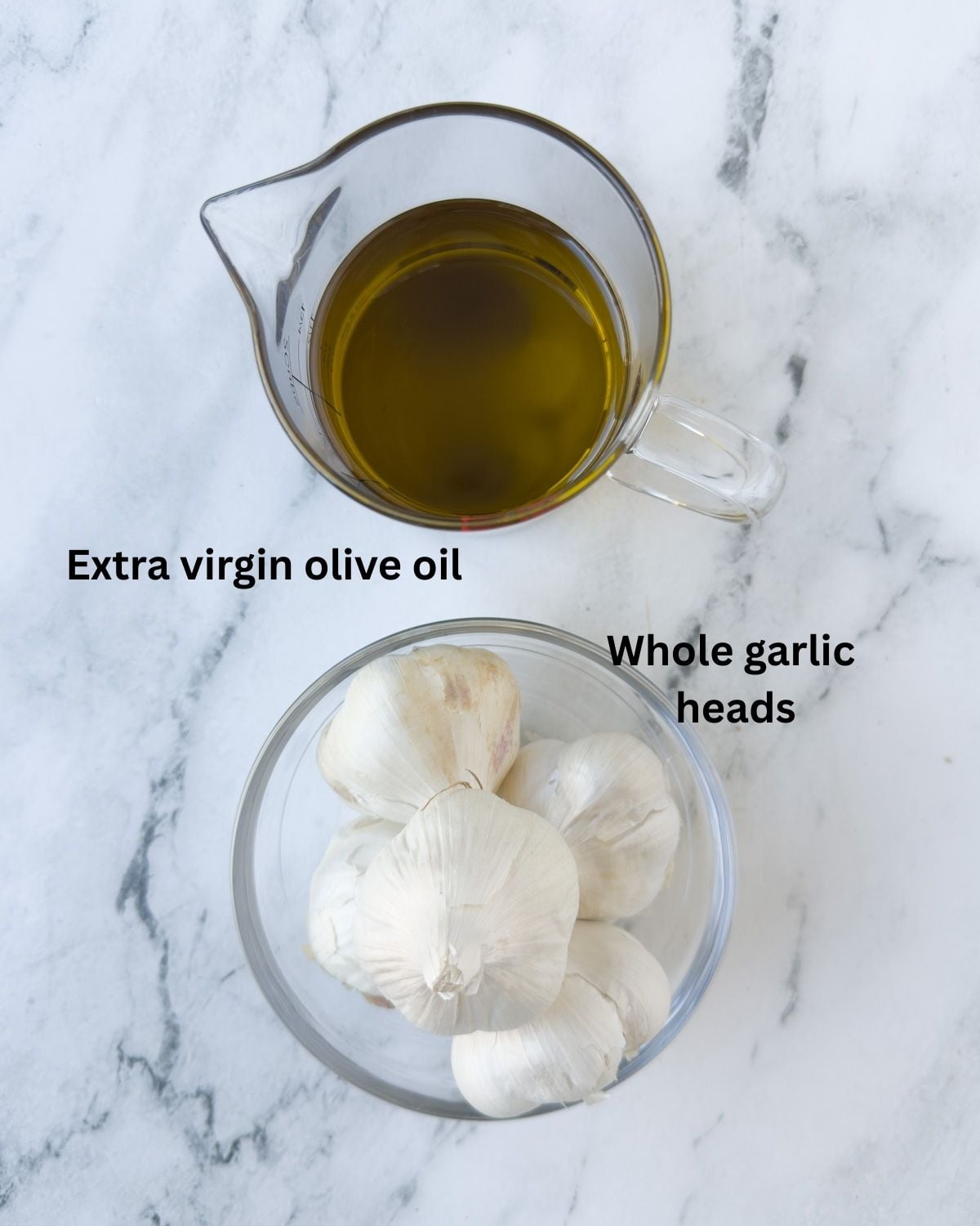 Two simple ingredients to make garlic confit: extra virgin olive oil and fresh garlic, on a counter.