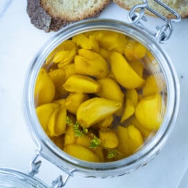A glass jar full of garlic confit cloves in gold olive oil with baguette slices.