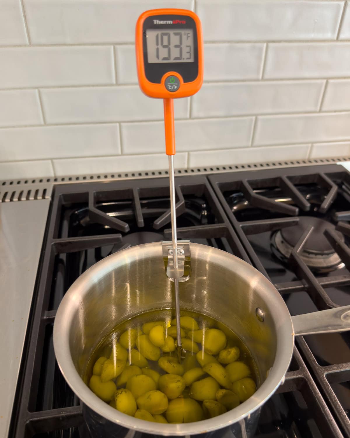 A small pot of garlic cloves cooking for garlic confit with an inserted digital thermometer to watch temperature.