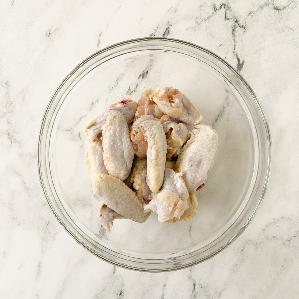 Chicken wing parts being oiled before seasoning, in a glass bowl.