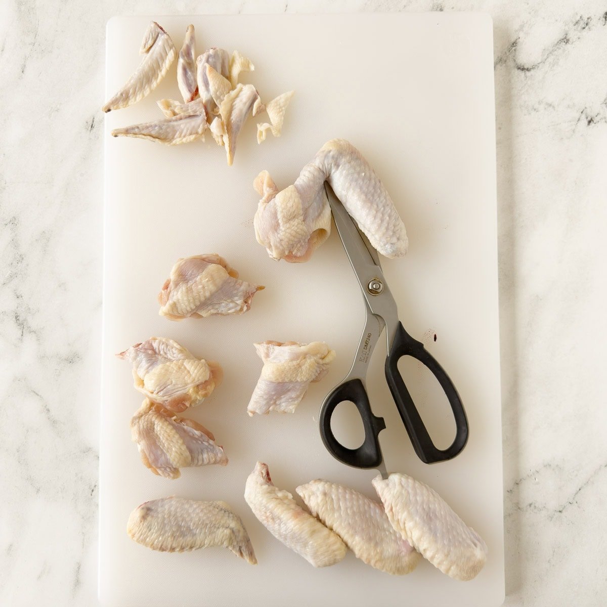 Cutting whole chicken wings into flats and drumettes with kitchen shears for baked wings.