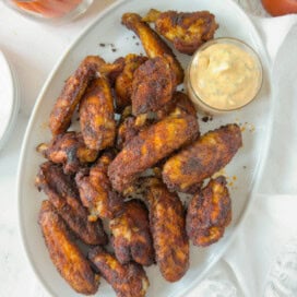 platter of oven baked chicken wings piled high with a buffalo ranch dressing in a small bowl.