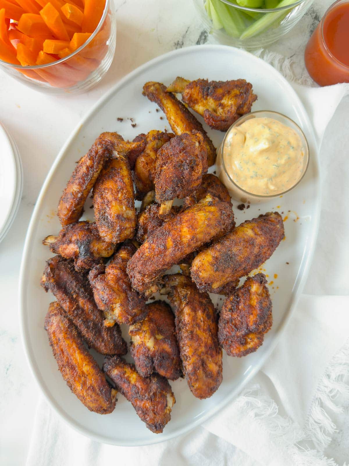 A platter of crisp seasoned oven baked chicken wings with carrots, celery and sauces. 
