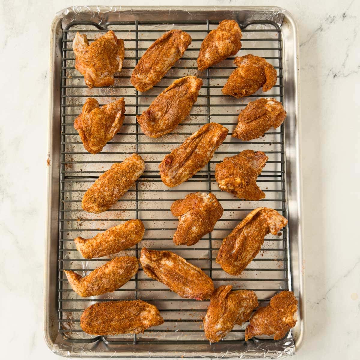 Party wings ready for baking arranged on a wire rack over a sheet pan.