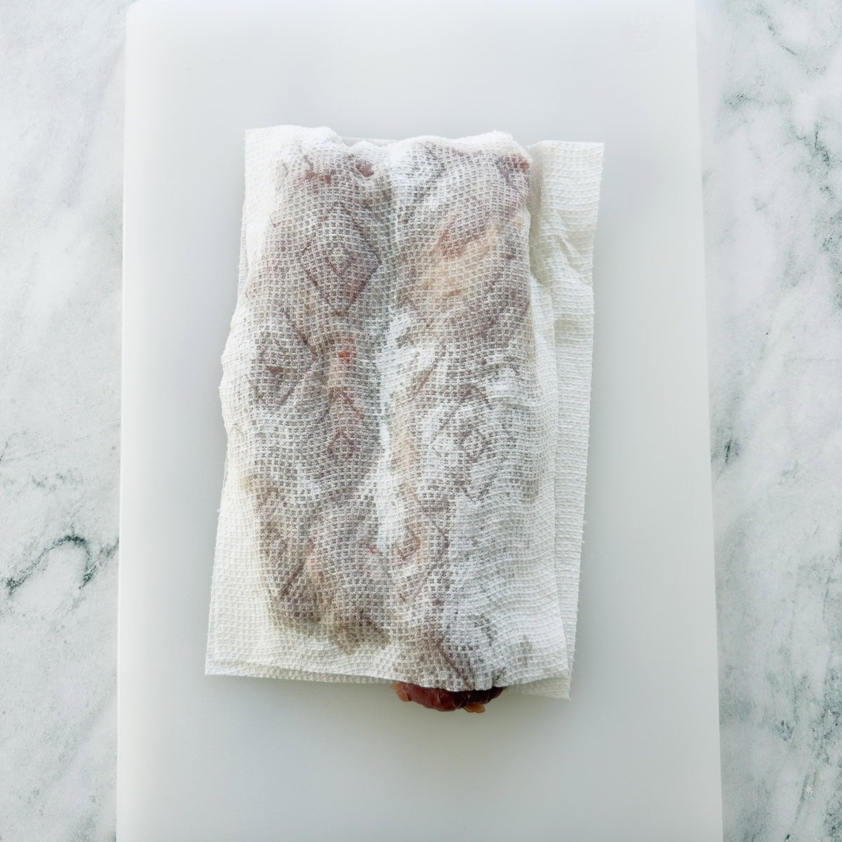 Drying pork tenderloin well for seasoning and searing on a white cutting board.