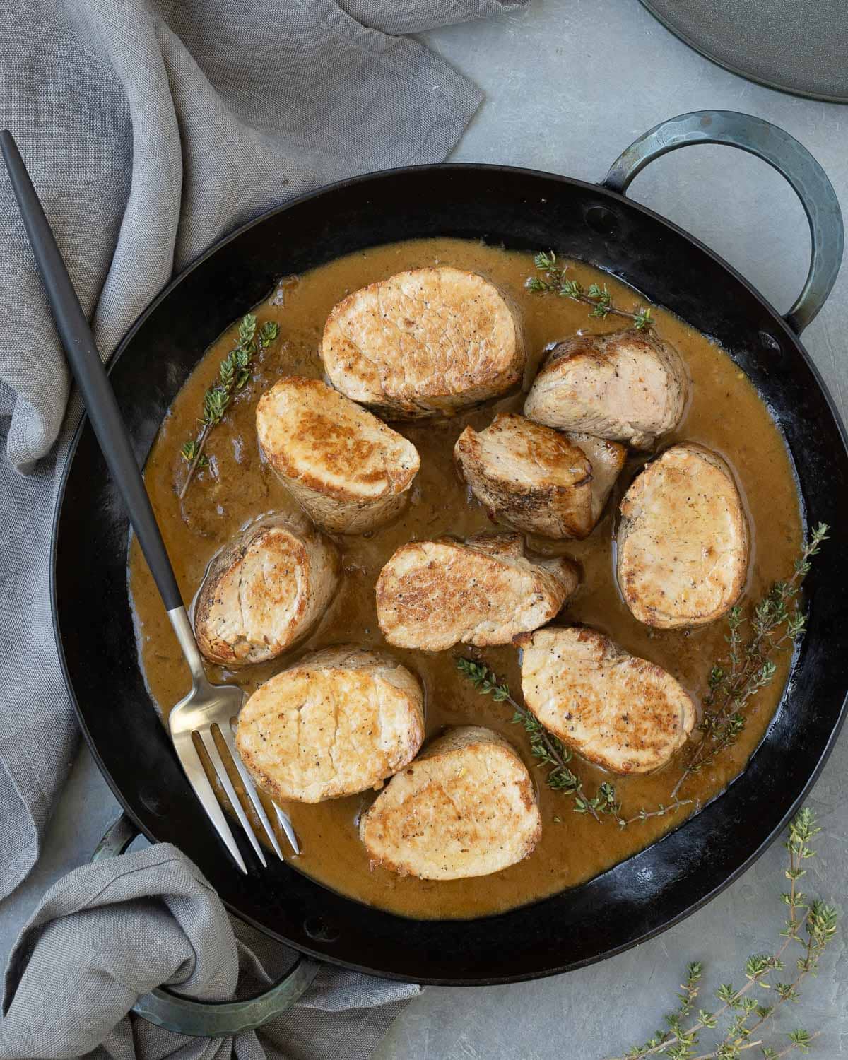 Seared pork tenderloin medallions in a black pan surrounded with creamy brown pan sauce.