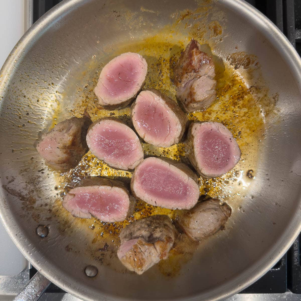 Pork medallion pieces searing briefly in a hot skillet to brown top side.
