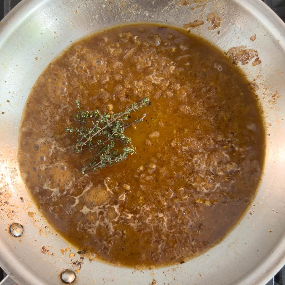A browned pan sauce cooking down with thyme sprigs for flavor.