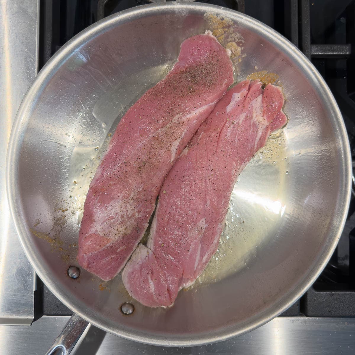 Searing pork tenderloins in a stainless steel wide skillet.