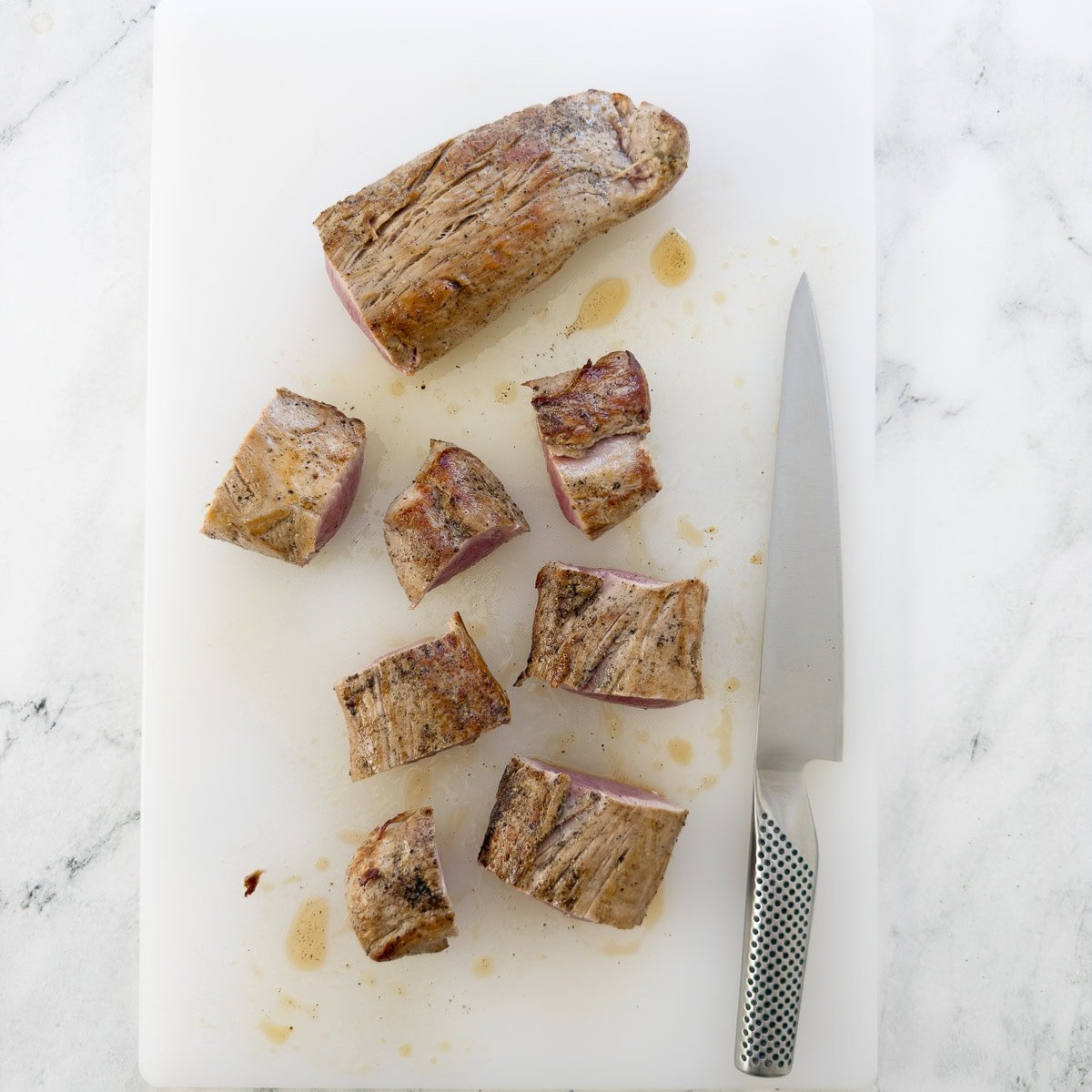 Slicing pork into medallions on a cutting board.
