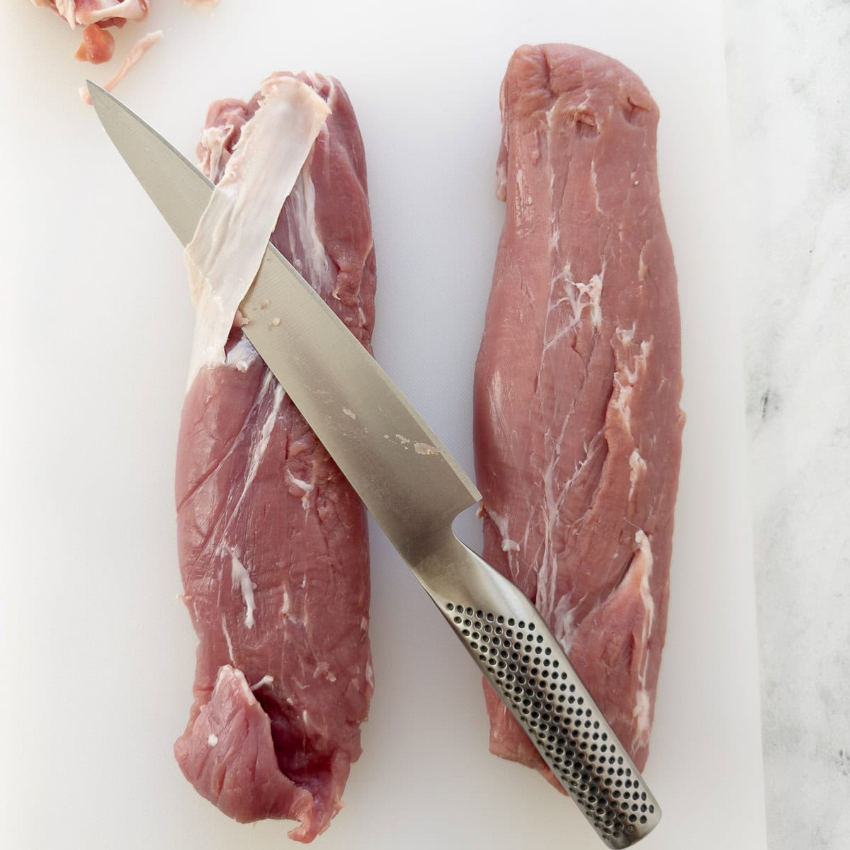 Trimming pork tenderloins of extra fat and silverskin with a knife.