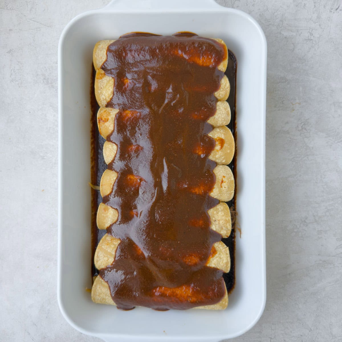 A baking dish fill of shredded beef enchiladas covered with brick red enchilada sauce.