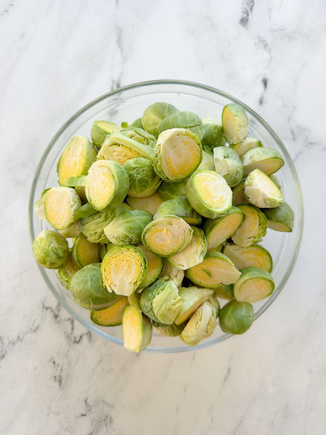 A glass bowl of trimmed and halved Brussels sprouts.