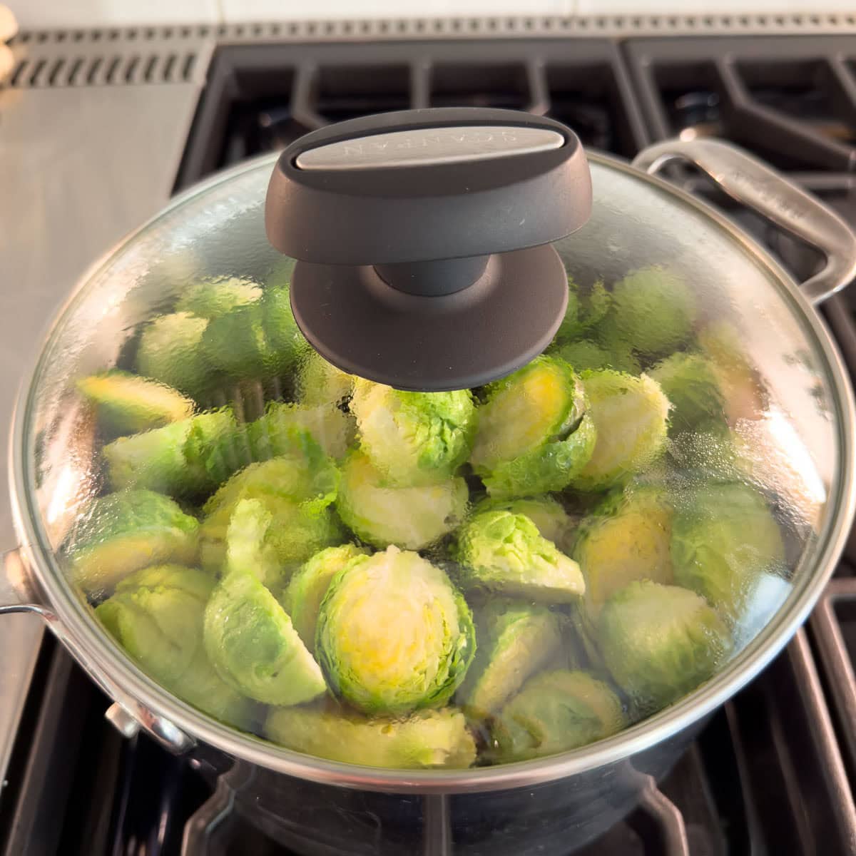Steaming Brussels sprouts in a pan seeing through a glass lid on the stovetop.