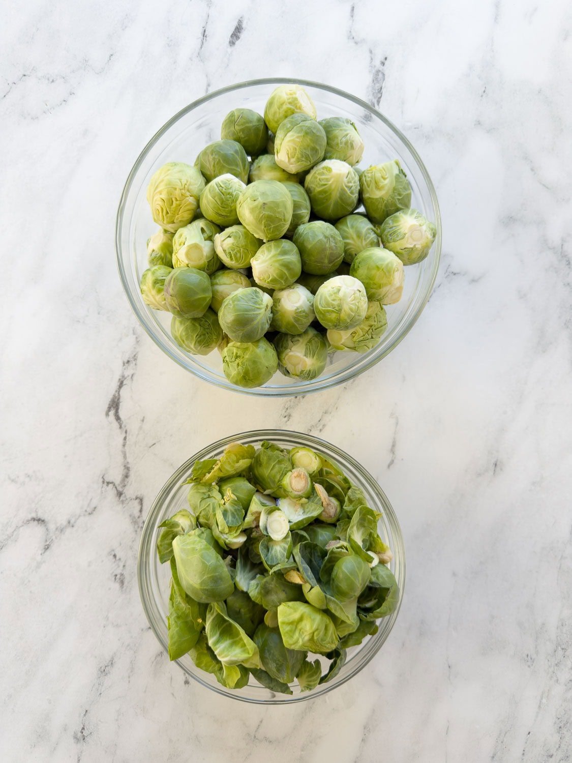 Bowls of trimmed Brussels sprouts and the trimmings on a counter.