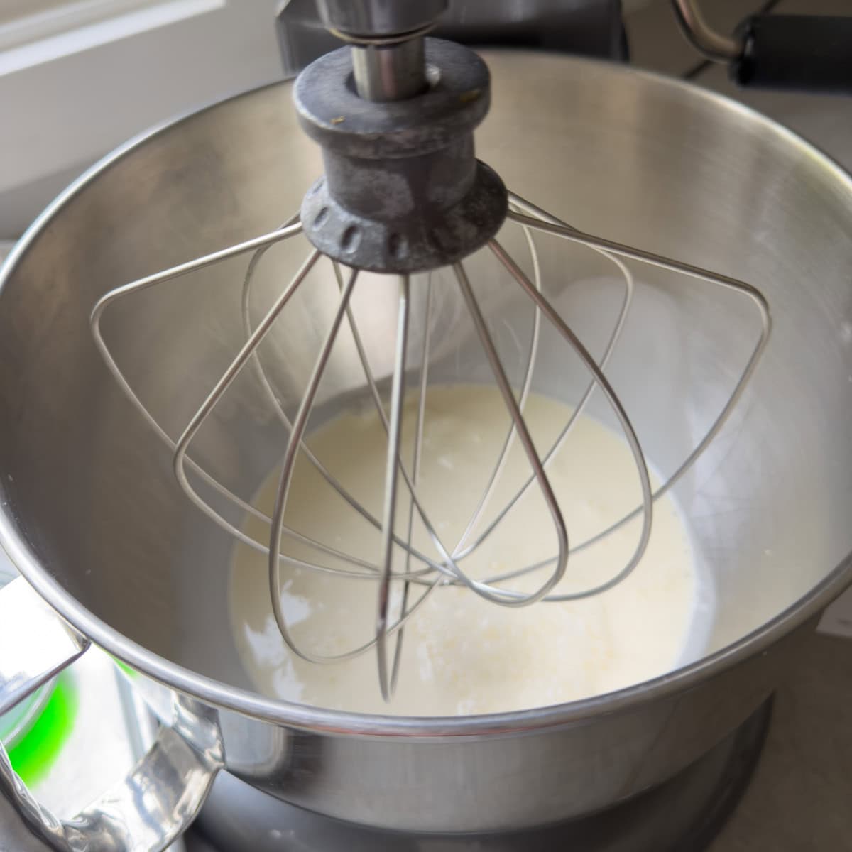 Heavy cream in the bottom of a standing mixer with the whip attachment, ready for whipping.