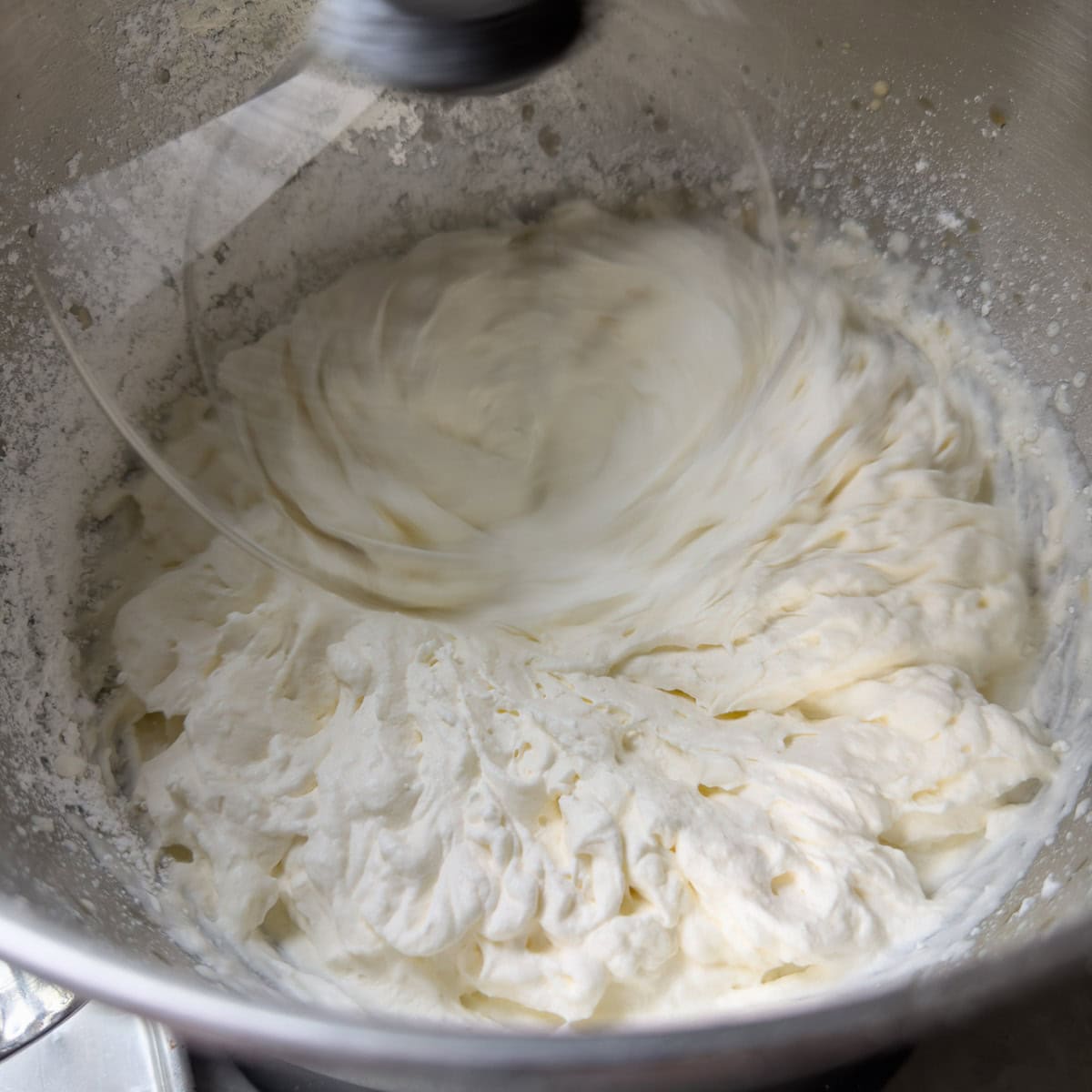 Whipped cream in the workbowl of a standing mixer.
