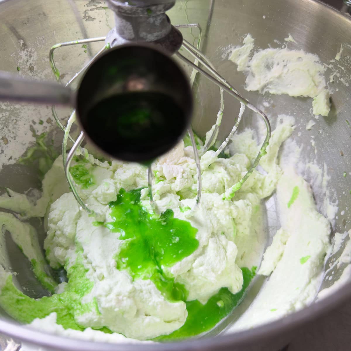 Bright green creme de menthe being poured into whipped cream for grasshopper pie filling.