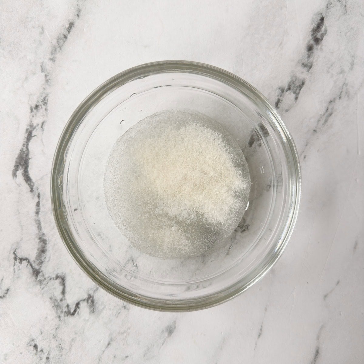 A small bowl of water and gelatin powder blooming.