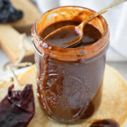 A jar of deep red enchilada sauce with a spoon on the top.