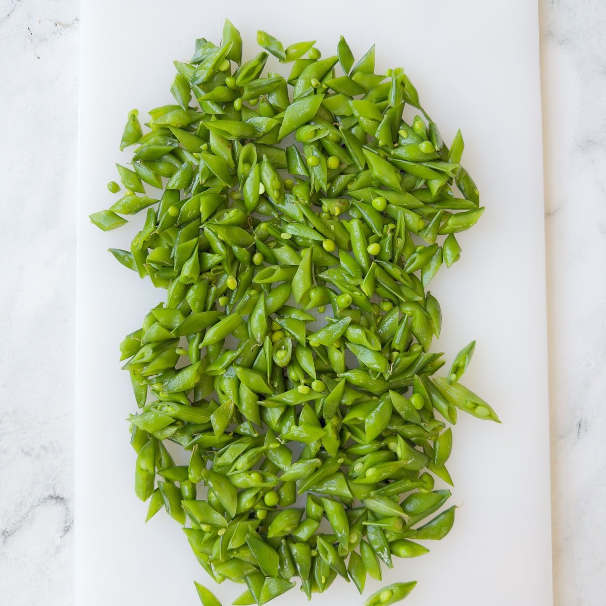 Chopped sugar snap peas on a white cutting board.