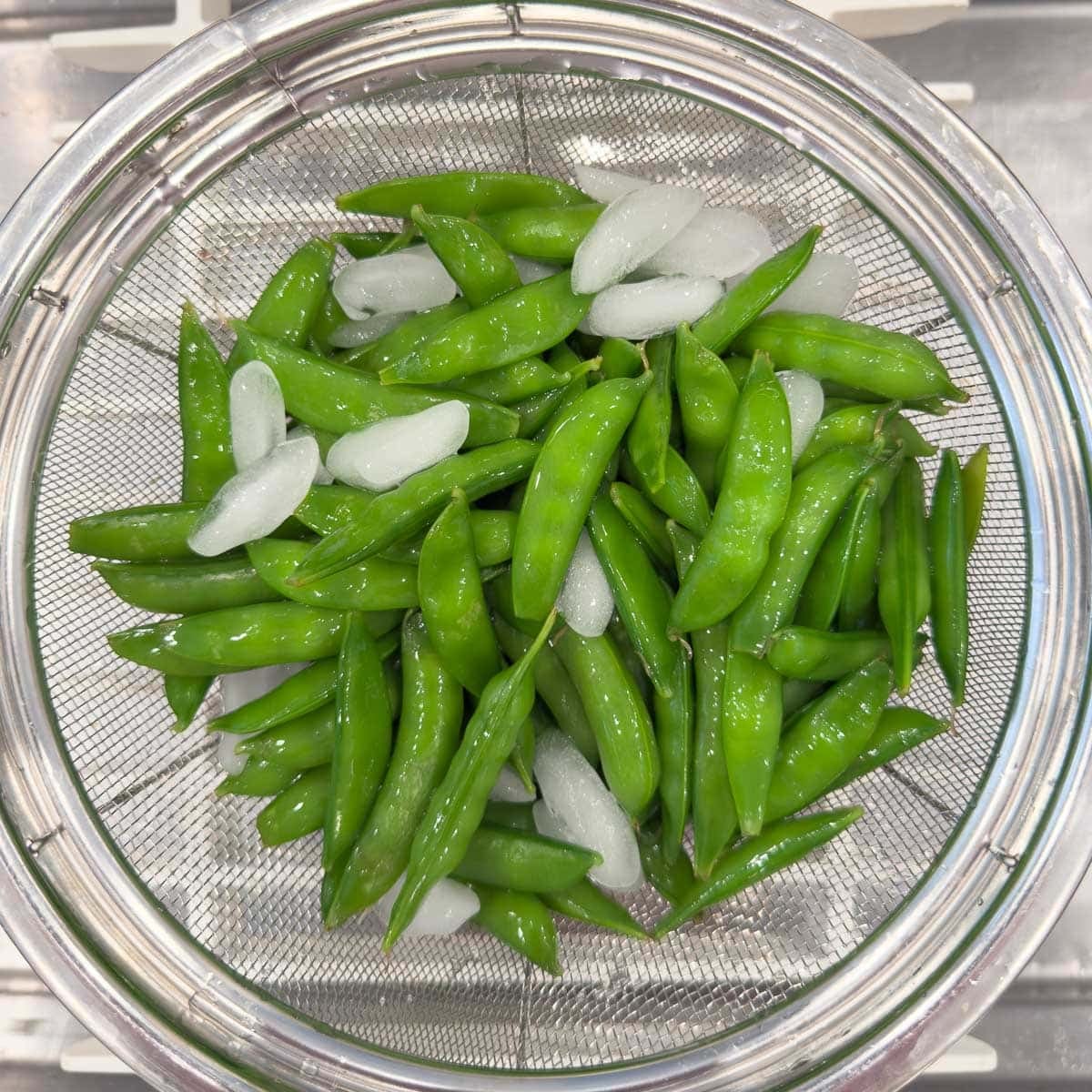 Draining snap peas in a silver colander in a sink.