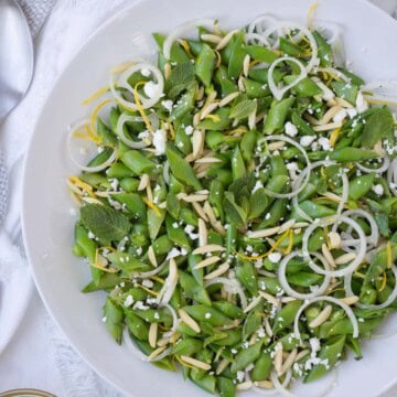 Emerald green snap pea salad with shallot, lemon and mint in a white bowl.