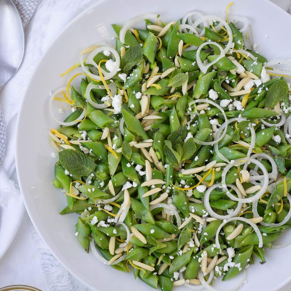 Emerald green snap pea salad with shallot, lemon and mint in a white bowl.