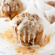 A golden cinnamon muffin with dripping glaze on a muffin paper.