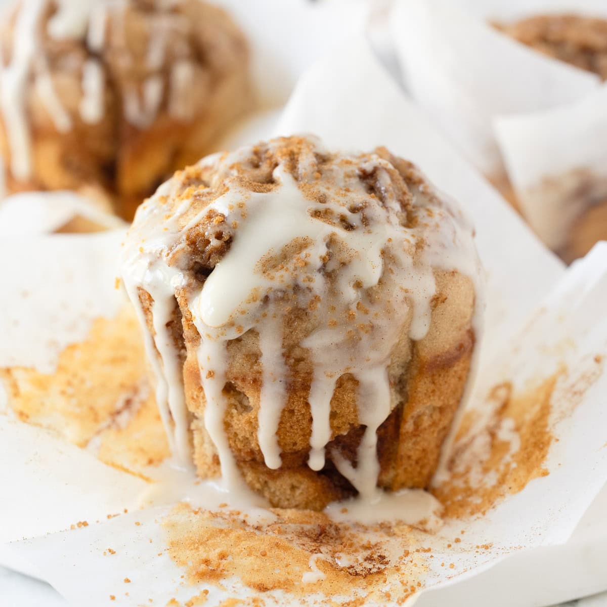 A golden cinnamon muffin with dripping glaze on a muffin paper.