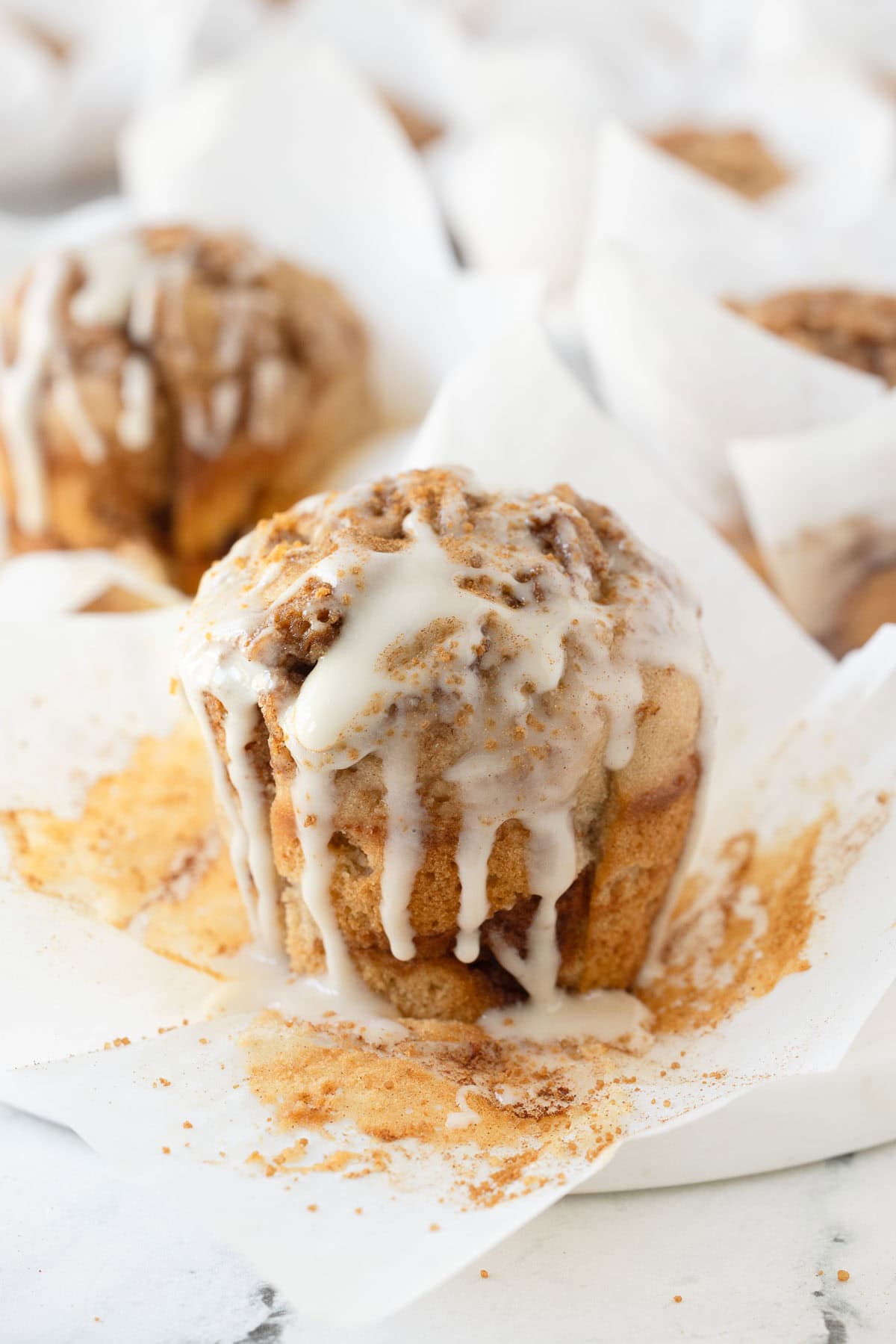 A cinnamon muffin with papar torn back drizzled with white icing. 