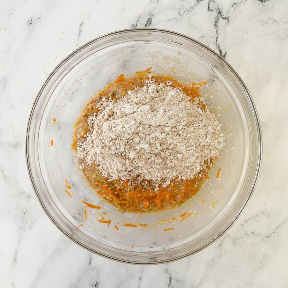 Adding dry ingredients to wet ingredients for a carrot cake batter.