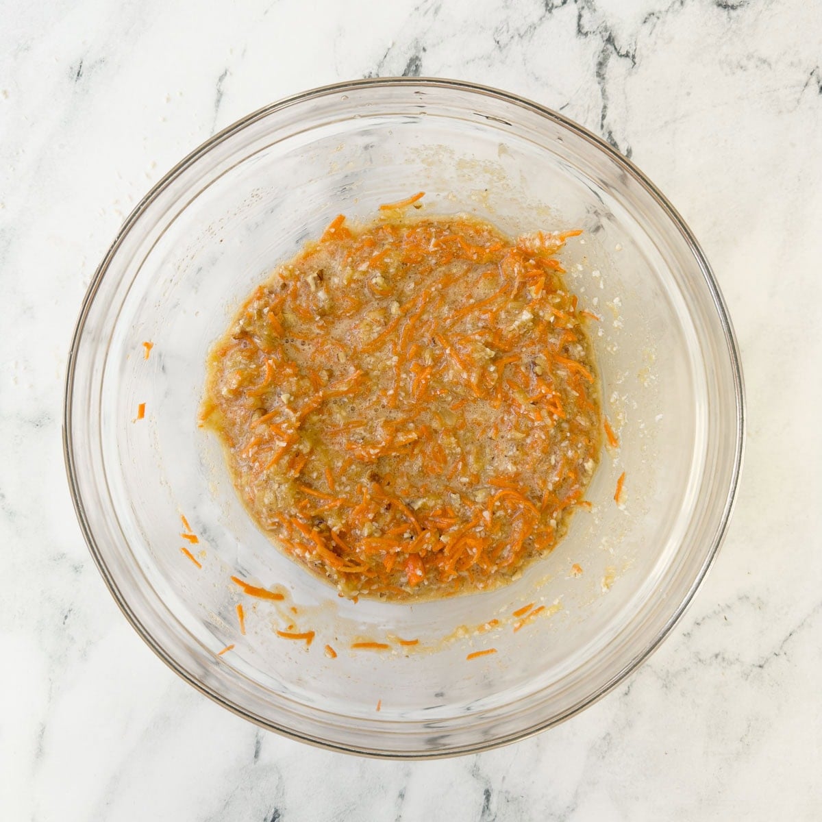 Cake batter with carrots, pineapple, and coconut in a glass bowl.