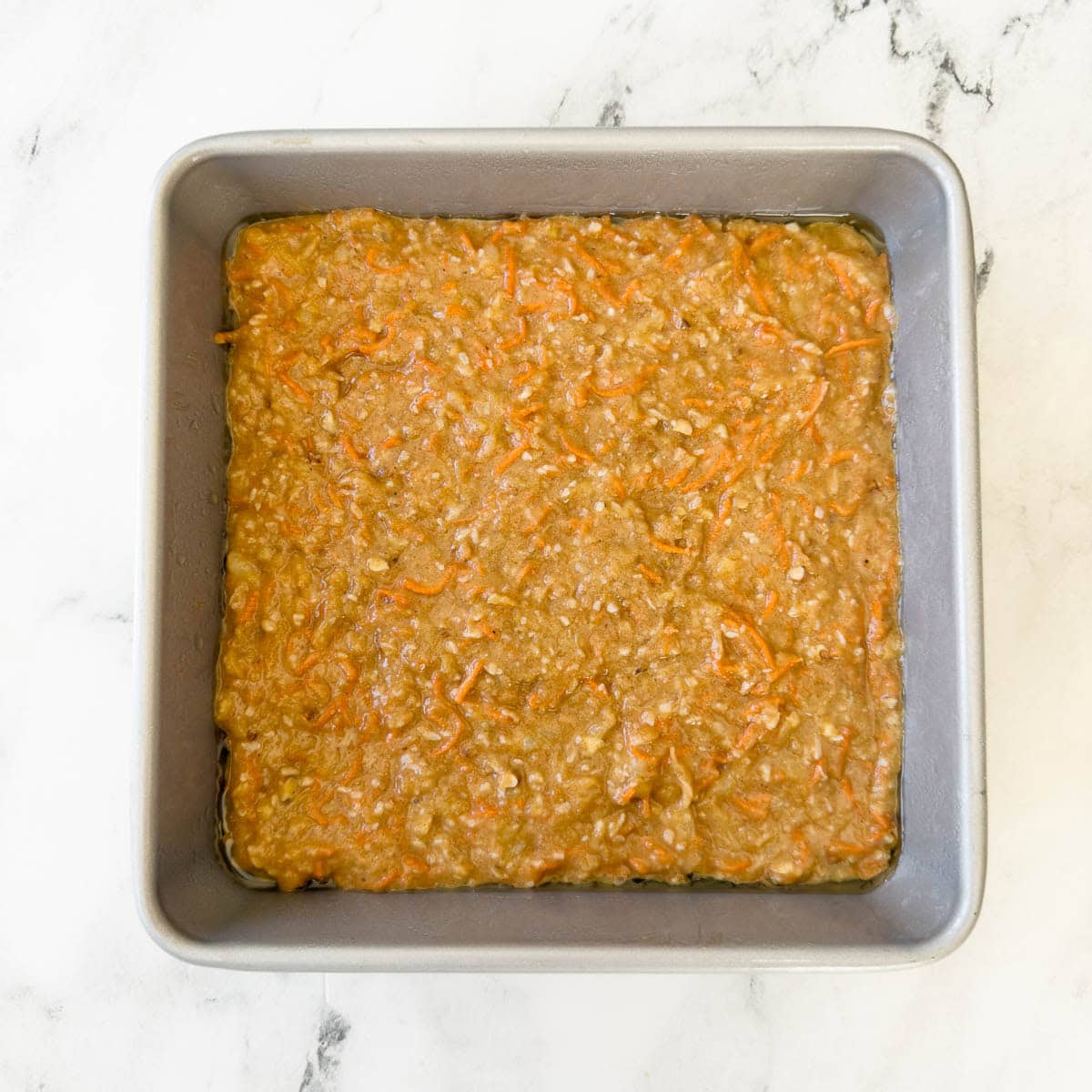 Carro cake batter poured into a square metal cake pan for baking.