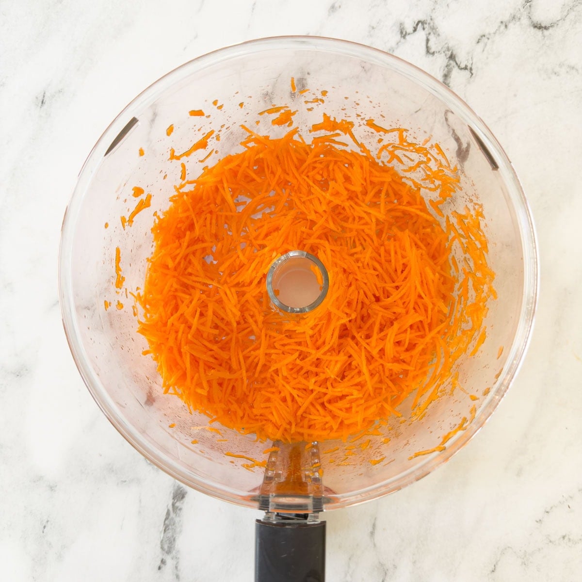 Finely grated orange carrots in a food processor workbowl.