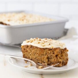 Carrot cake with cream cheese frosting and chopped nuts on a plate with a fork.