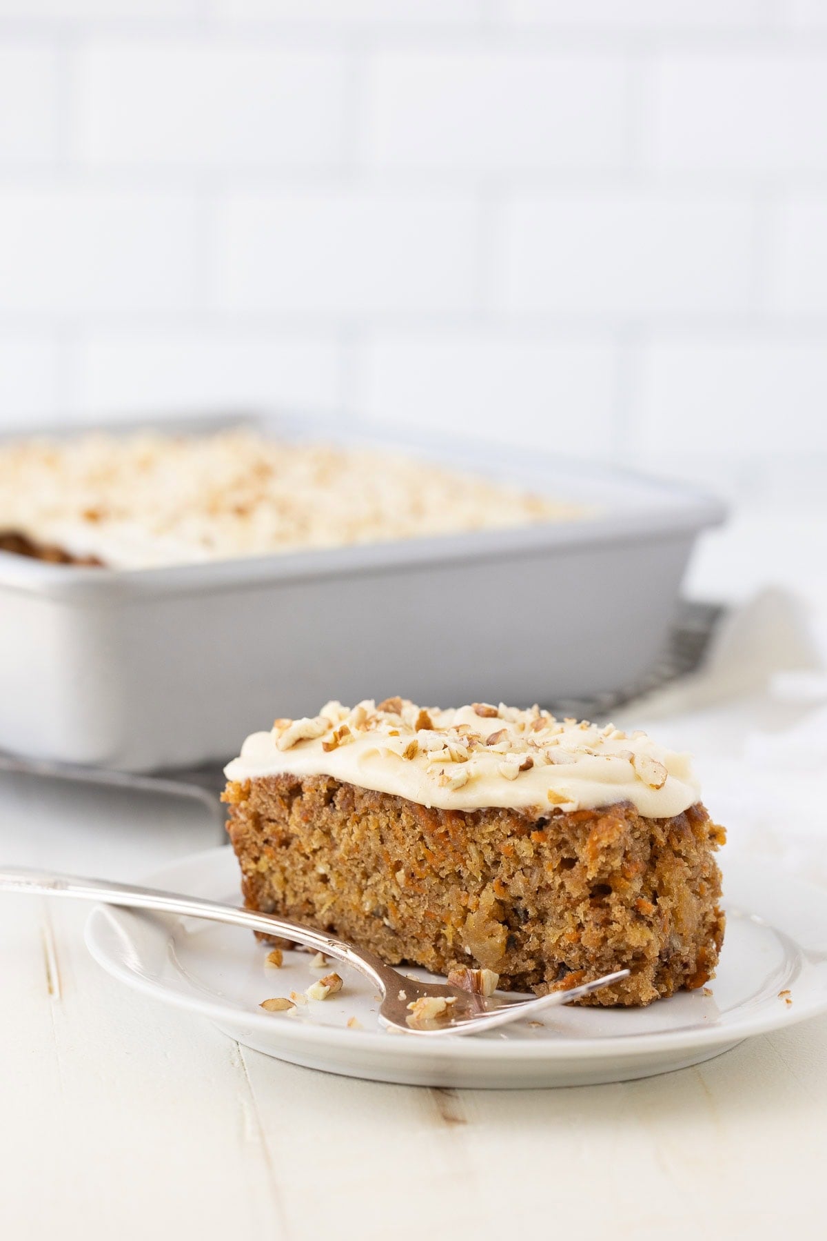 A slice of gluten-free carrot cake with cream cheese frosting sprinkled with nuts.