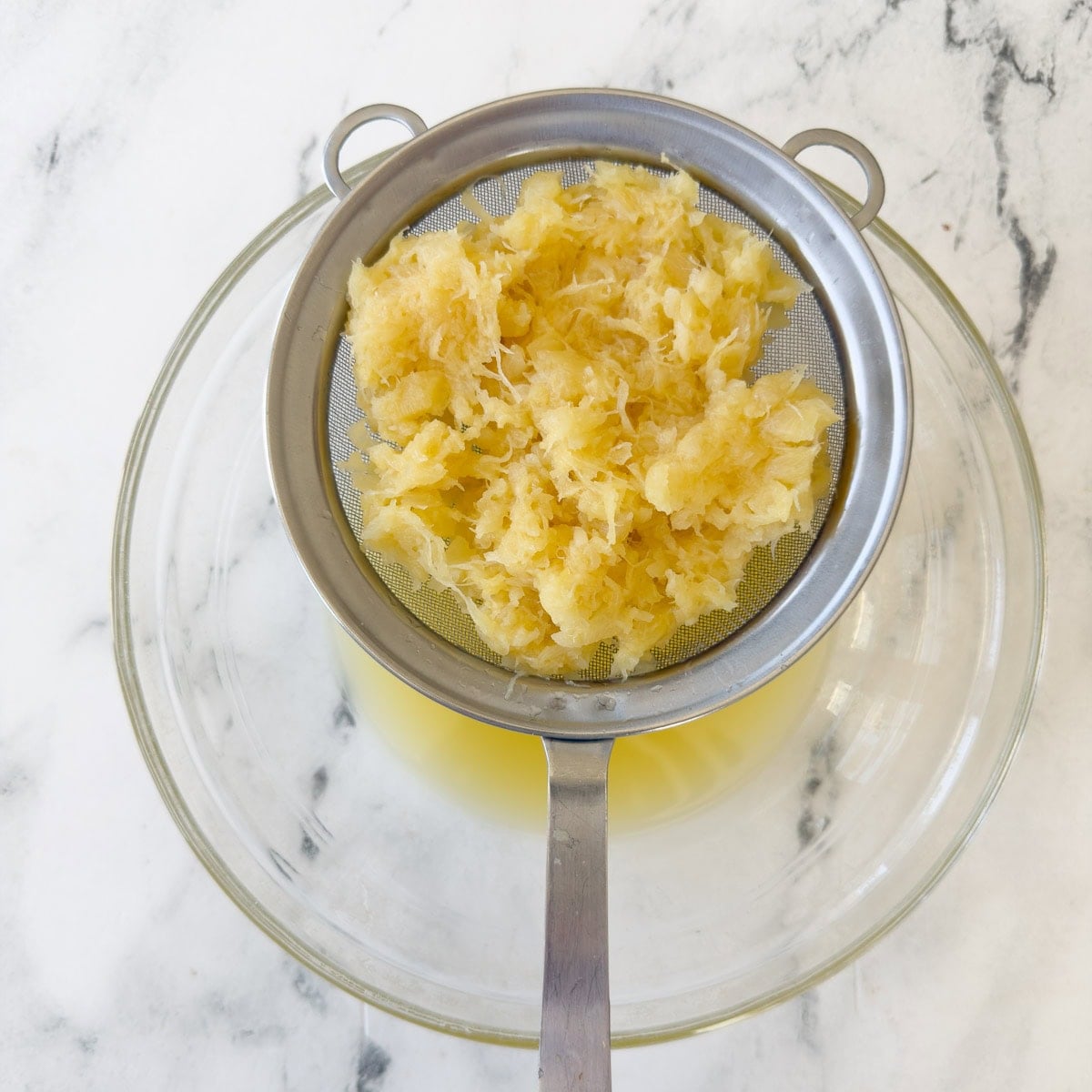 Draining crushed pineapple through a sieve into a bowl.