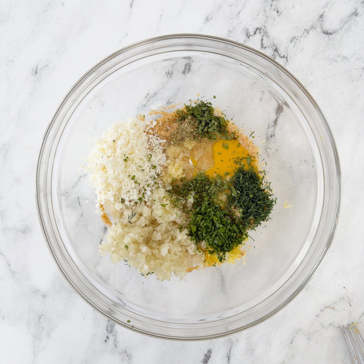 Glass bowl with egg, herbs, onion, breadcrumbs and milk for a meatball base mix.