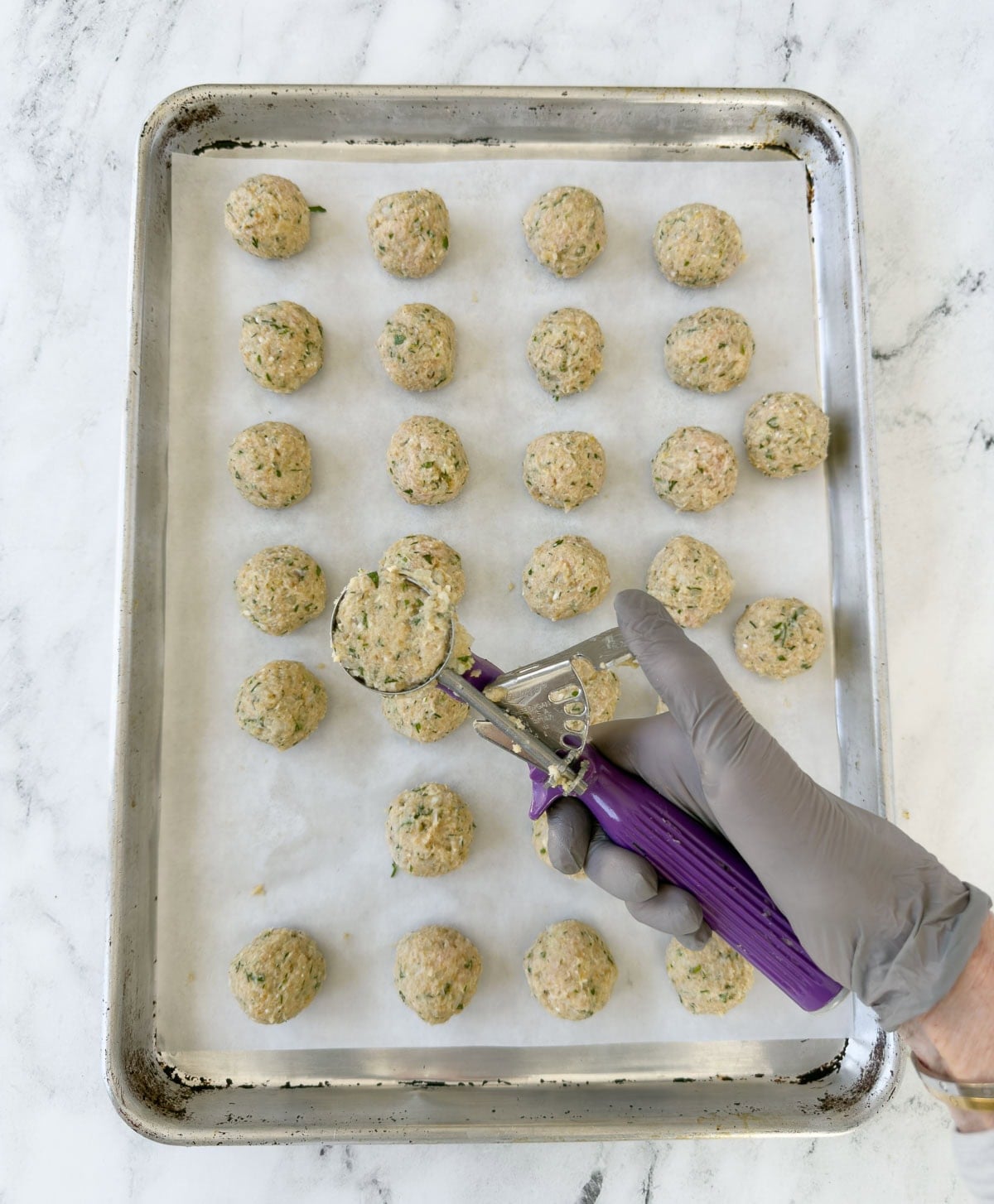 Portioning Greek chicken meatballs mix onto a baking tray with a scoop.