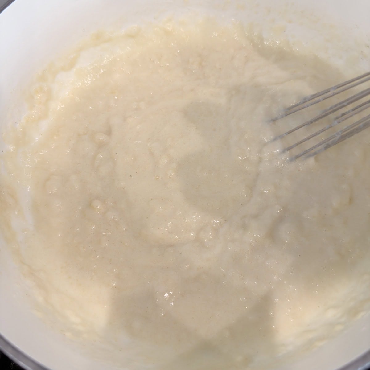 Cooking a white sauce in a pan on the stovetop, with a whisk.