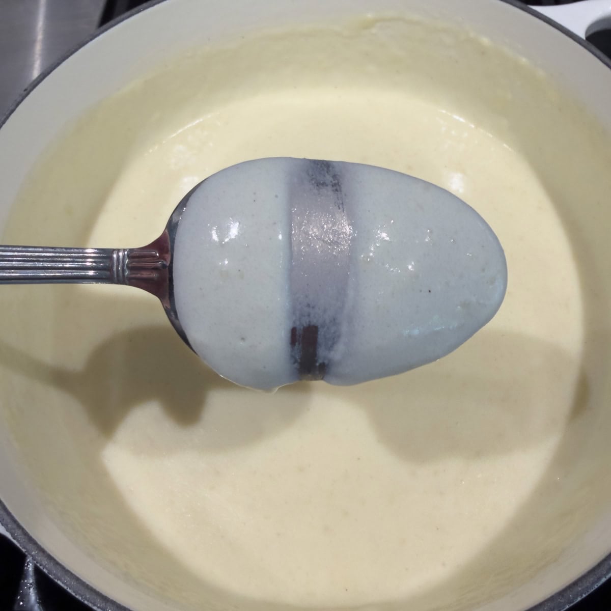 A finished bechamel sauce coating the back of a spoon as the thickness test.
