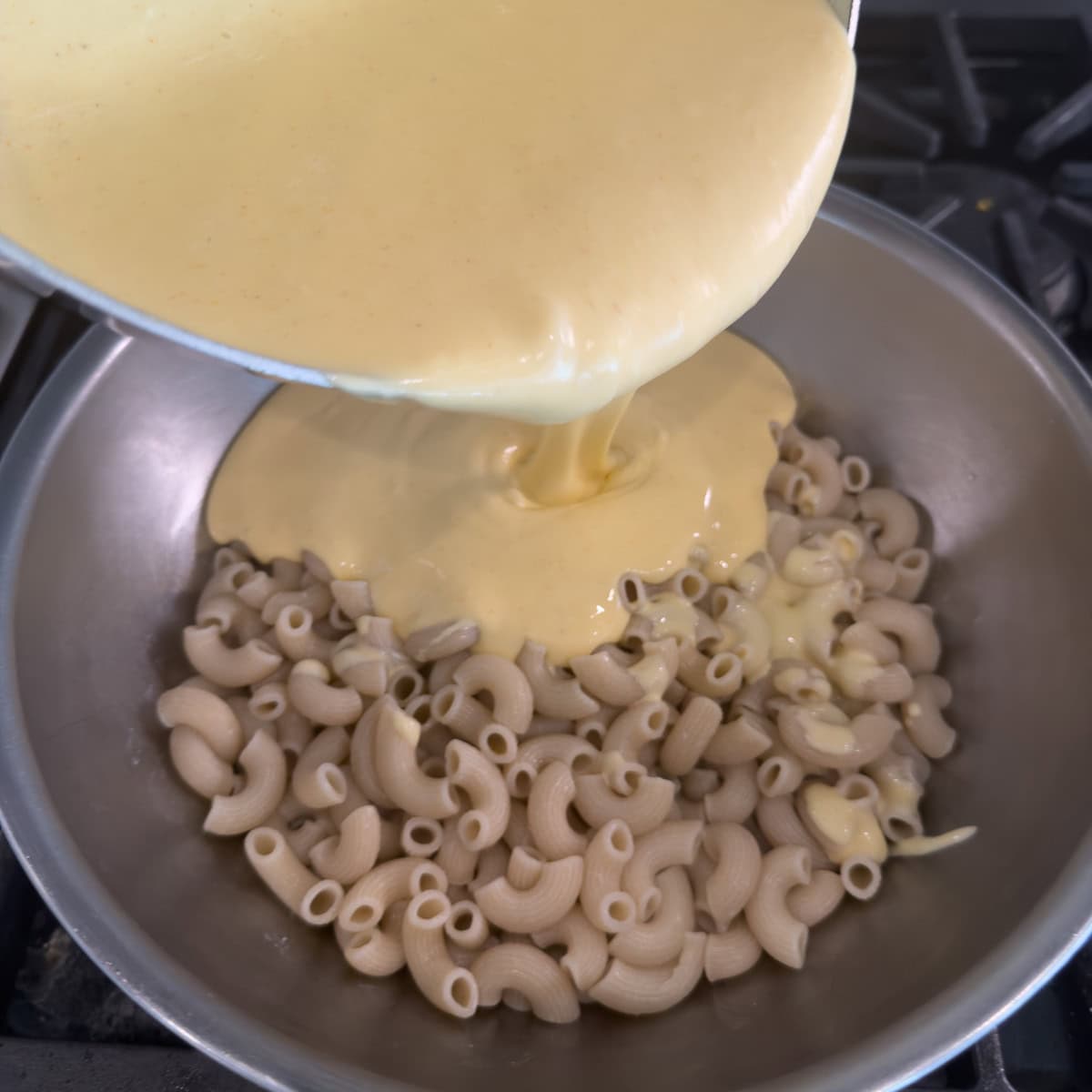 Pouring cheese sauce over cooked elbow macaroni for mac and cheese.
