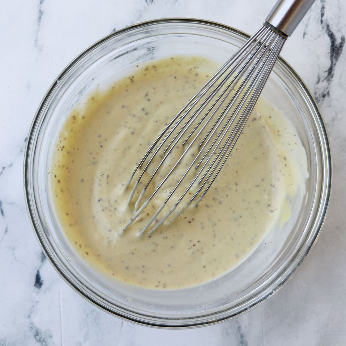 Finished Dijon aioli with a silver whisk in a glass bowl.