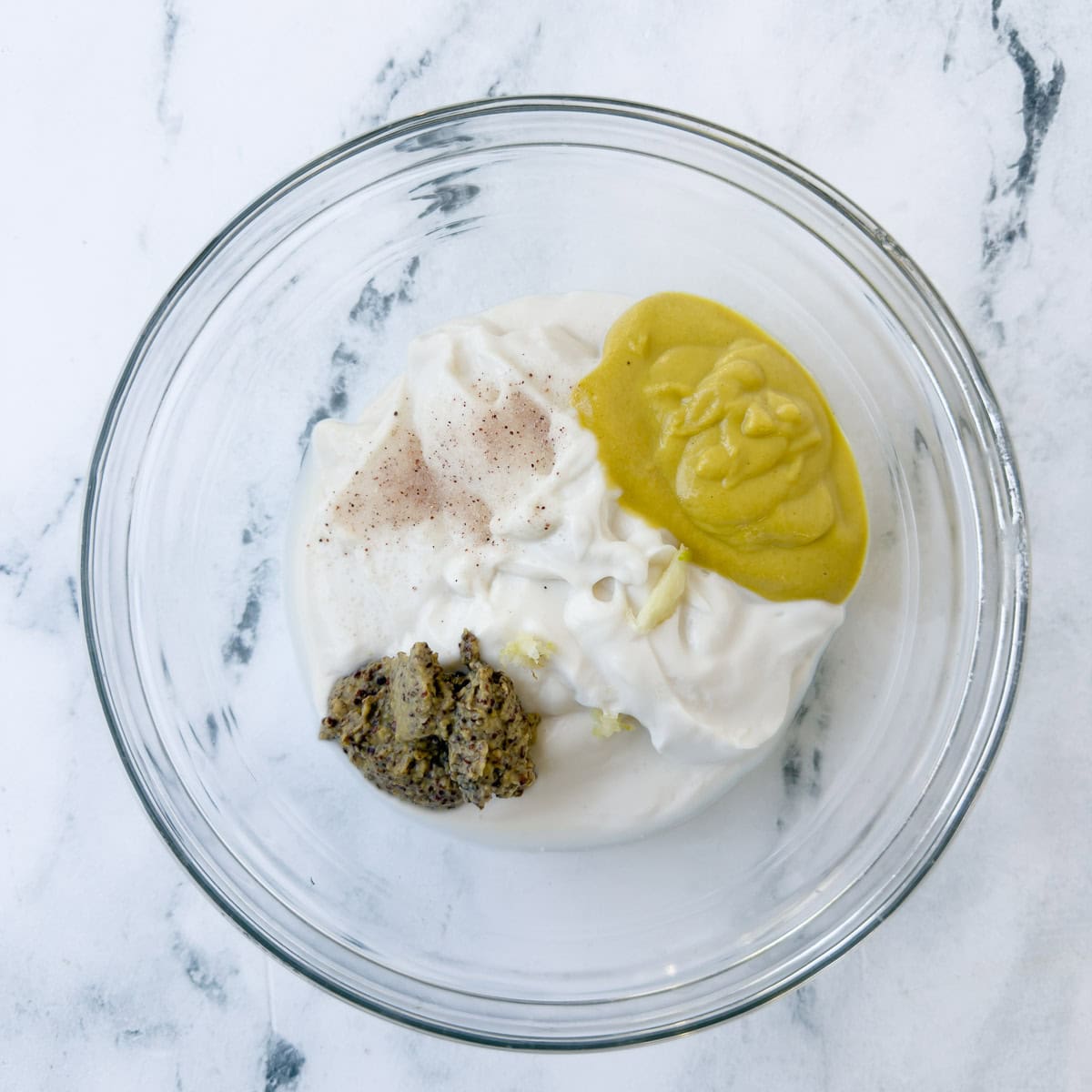 Ingredients for dijon mustard aioli sauce in a glass bowl for mixing.