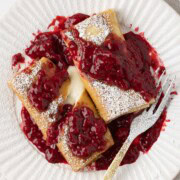 A plate of cheese blintzes with thick raspberry sauce and a fork.
