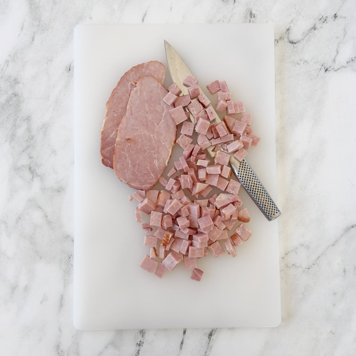 Chopped ham with a chefs knife on a white cutting board.
