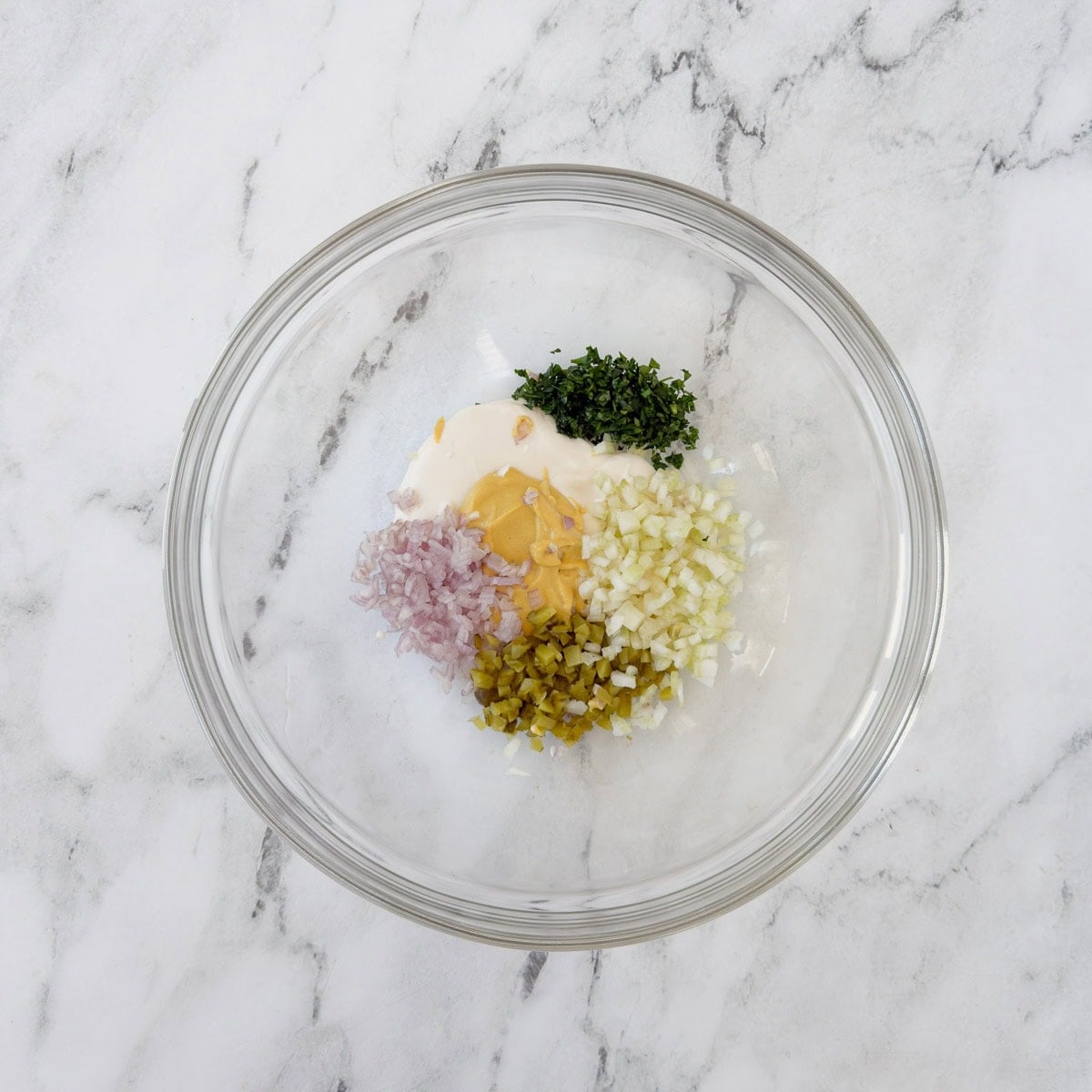 A glass bowl with ham salad dressing ingredients.
